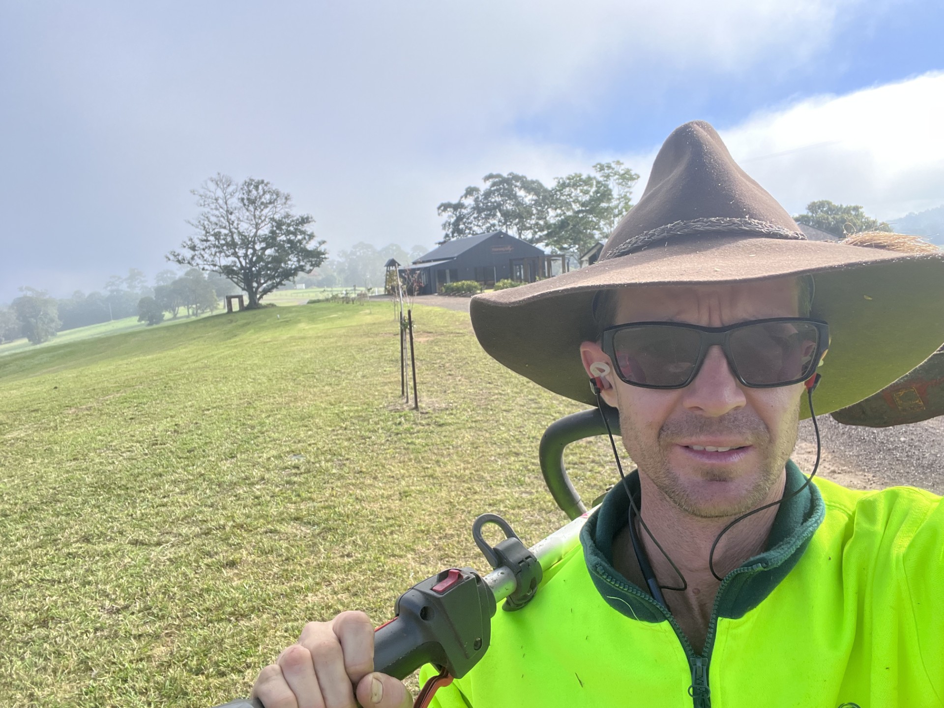 Mary Valley Mowing owner in a wide-brim hat carrying a line trimmer on a freshly mown acreage lawn