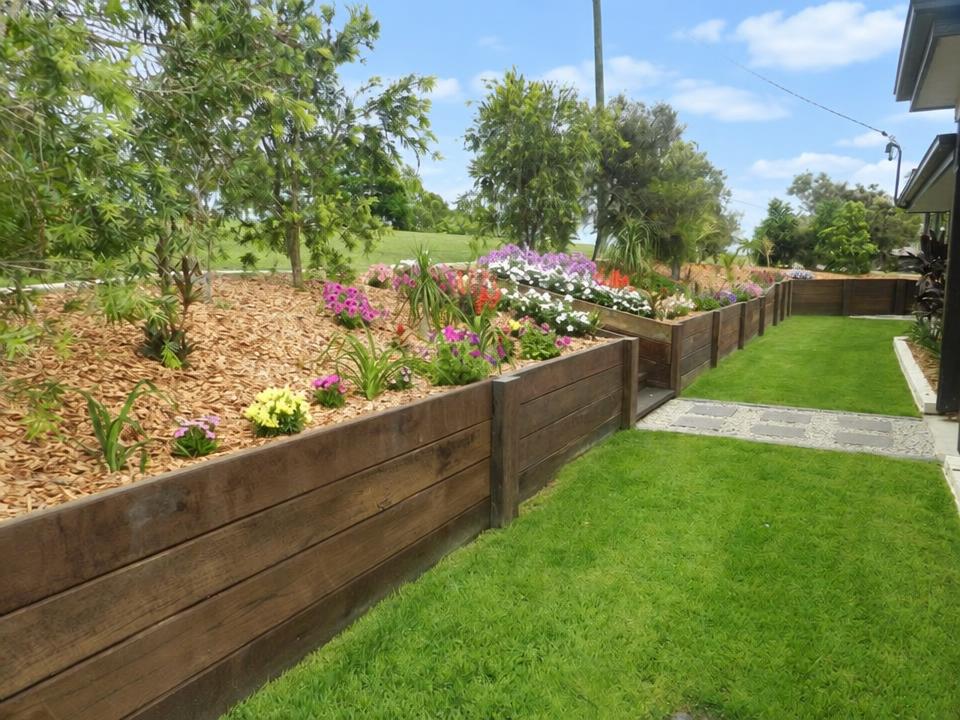 Timber-edged mulched garden beds full of flowers beside a freshly mown lawn